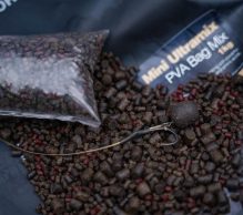 Close-up of a scattered pile of dark brown and red pellet mix with an empty, clear plastic bag on top, labeled 